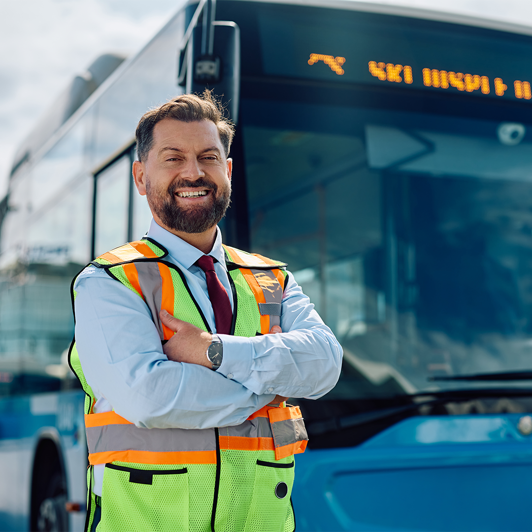 Fleet operator smiling and standing confidently in a safety vest in front of an electric bus.