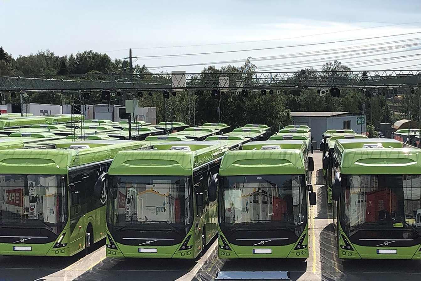Large fleet of green electric buses parked in a depot, illustrating the scale and reliability risk of growing charge operations.